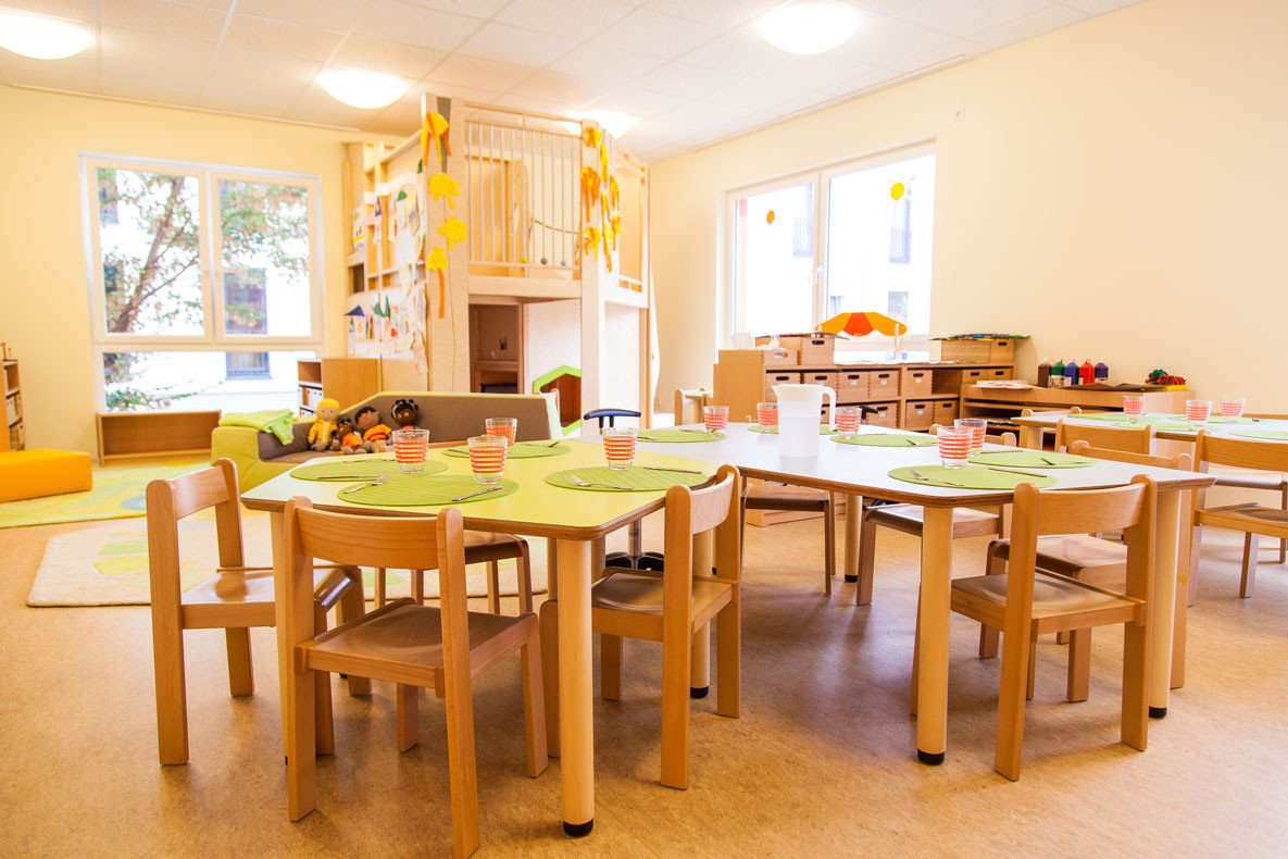 Heller Gruppenraum mit gedeckten Kindertischen.