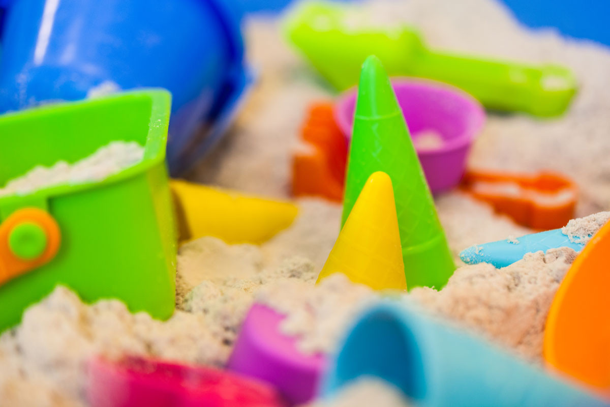 Bunte Sandspielzeuge wie Förmchen, Eimer und Schaufel liegen im Sand.