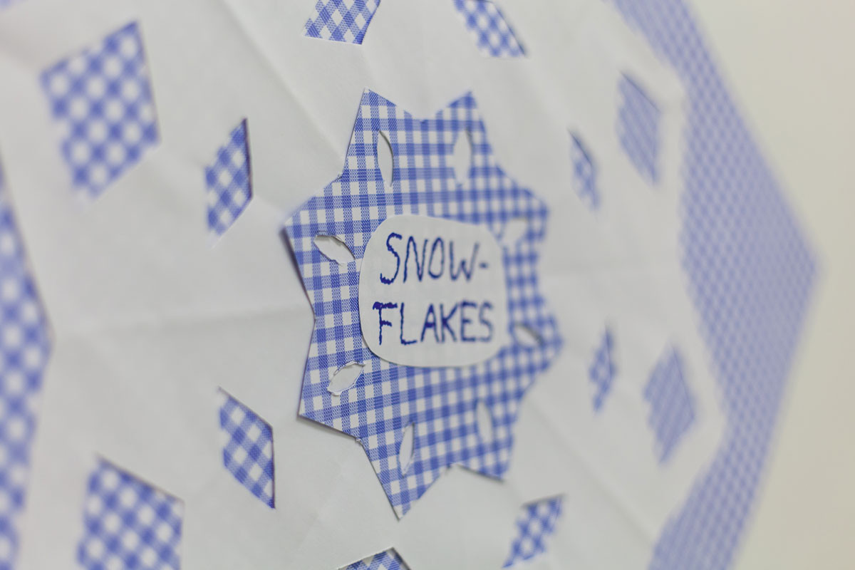 Gebasteltes Schneeflockenmuster aus blau-weiß kariertem Papier mit der Auschrift "Snowflakes".