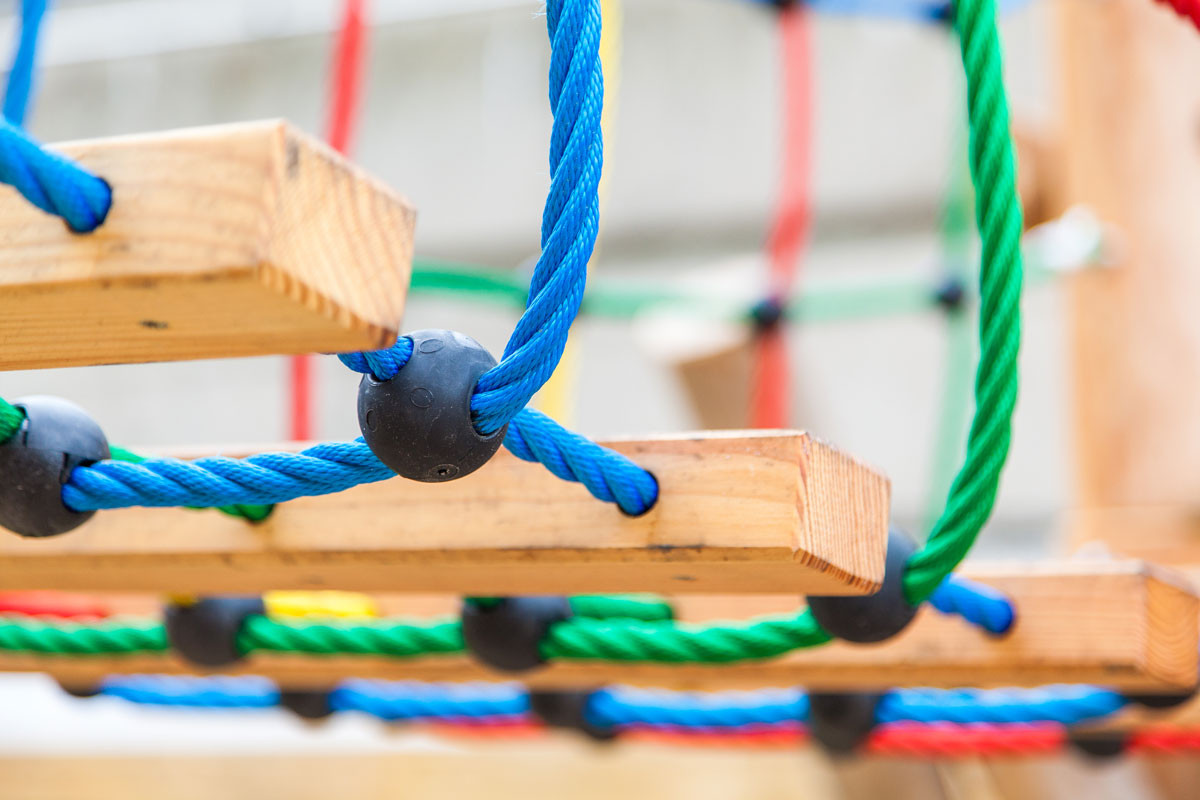 Detailaufnahme einer Kletterbrücke aus Holzsprossen und bunten Seilen.