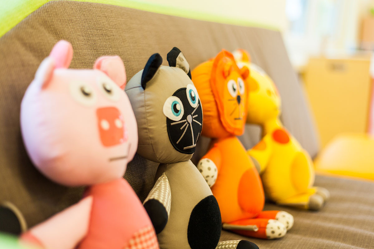 Vier bunte Stofftiere sitzen nebeneinander auf einem Sofa.
