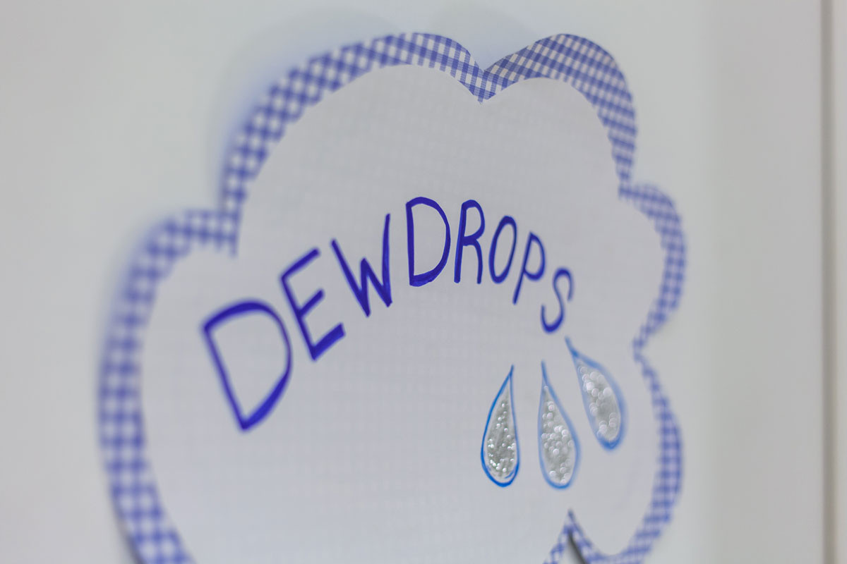 Gebastelte Wolke aus blau-weiß kariertem Papier mit der Aufschrift "Dewdrops" und drei gemalten Tautropfen.